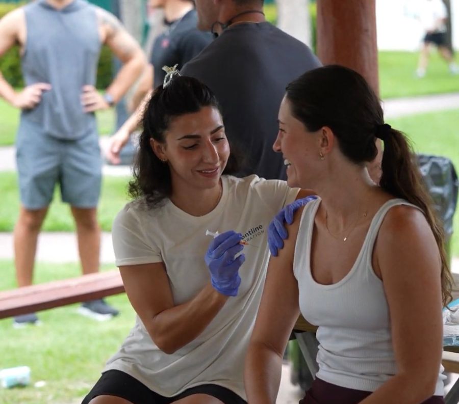 Frontline Hydration provider giving a smiling client a wellness shot at an outdoor event